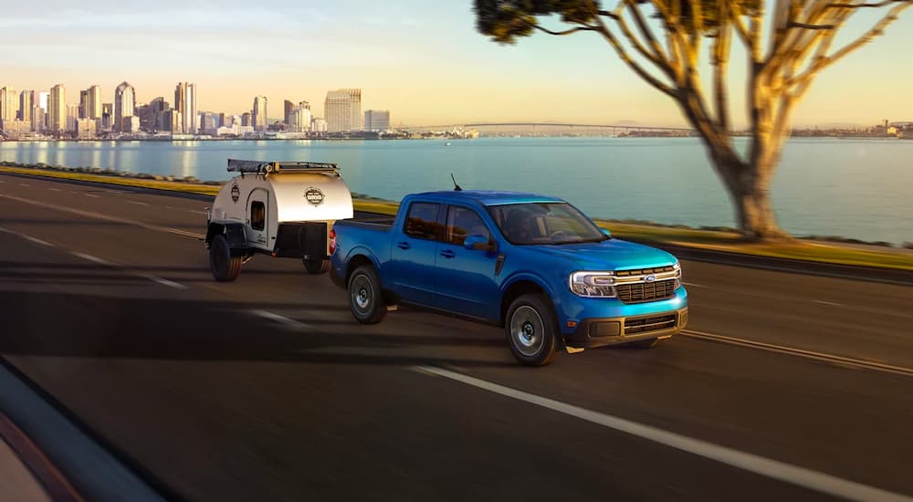 A blue 2022 Ford Maverick is shown towing a teardrop trailer after leaving a Ford dealership.