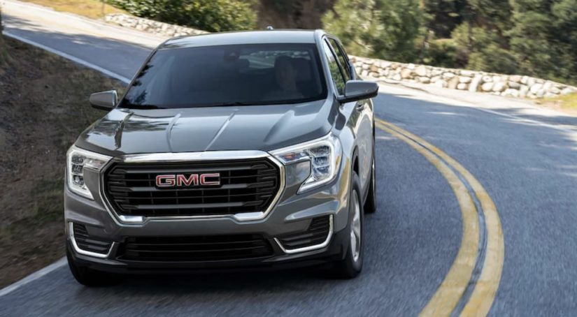 A grey 2023 GMC Terrain is shown driving on a two lane road.