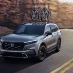 A silver 2023 Honda CR-V Hybrid Sport Touring is shown driving past rock faces.