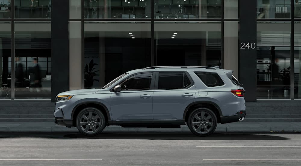 A grey 2023 Honda Pilot Sport is shown from the side driving on a city street.