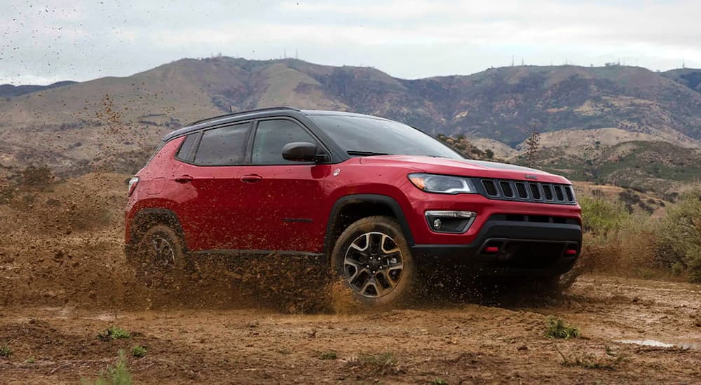 A red 2021 Jeep Compass Trailhawk is shown from the front at an angle while driving off-road.