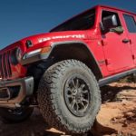 A red 2023 Jeep Wrangler Rubicon 392 is shown from the front while driving in a rocky area.