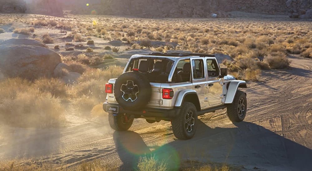 A silver 2023 Jeep Wrangler 4xe is shown from the rear while driving on a dirt trail after leaving a Jeep dealer.