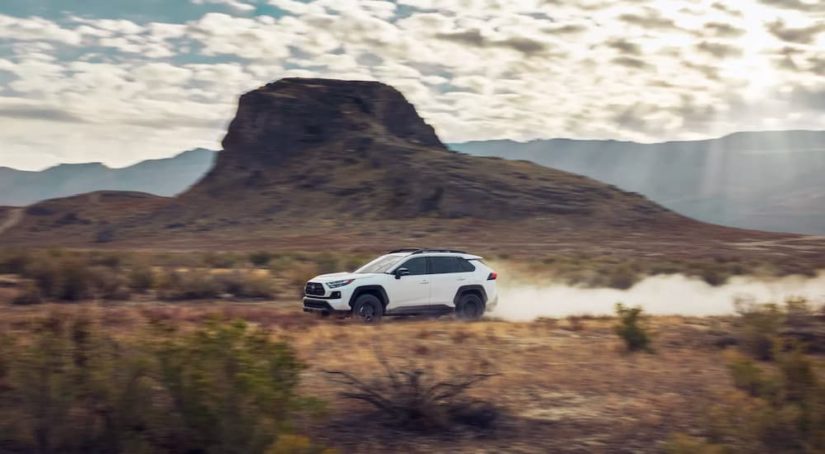 A white 2022 Toyota RAV4 TRD Off-Road is shown driving on a dusty trail.