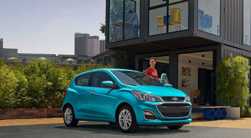 A teal 2021 Chevy Spark is shown parked outside of a modern house after leaving a used Chevrolet dealership.