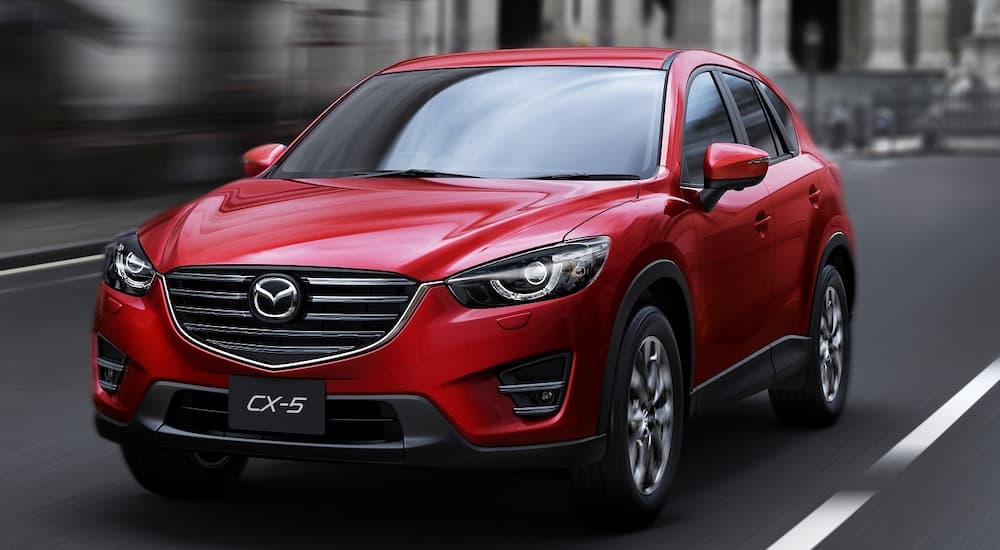 A red 2015 Mazda CX-5 is shown driving on a city street.