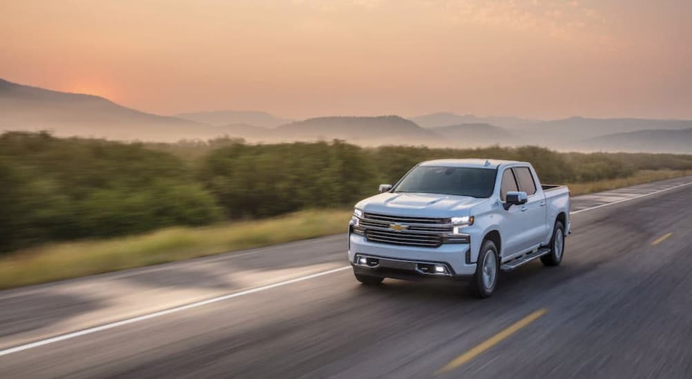 A white 2021 Chevy Silverado 1500 High Country is shown driving at sunset.