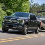 A black 2021 Ford F-150 Limited Hybrid is shown towing a boat.