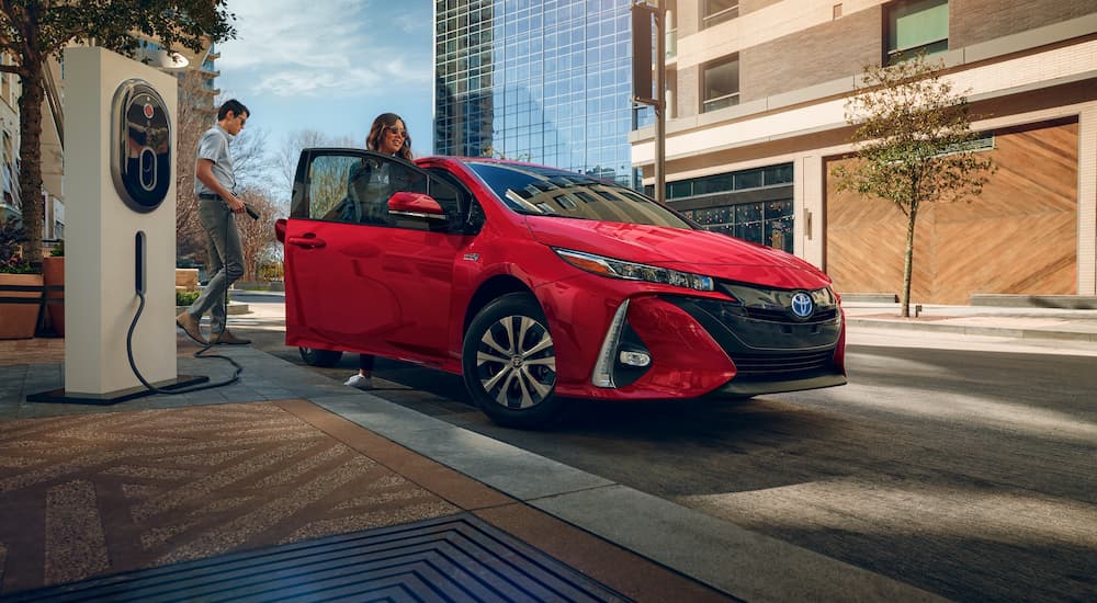 A red 2021 Toyota Prius Prime, a popular used hybrid car for sale, is shown parked at a charging station.