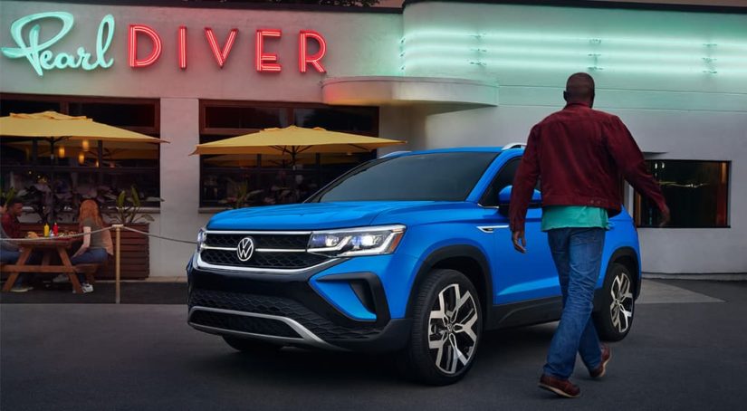 A man is shown walking towards the driver's side of a blue 2022 Volkswagen Taos.