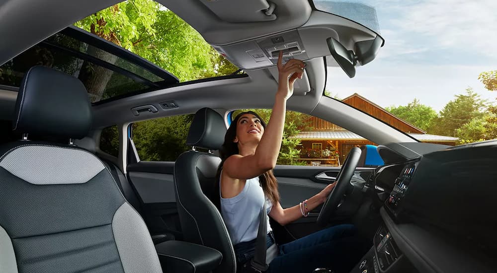 A woman is shown opening the sunroof of a 2022 Volkswagen Taos at a VW Taos dealer.