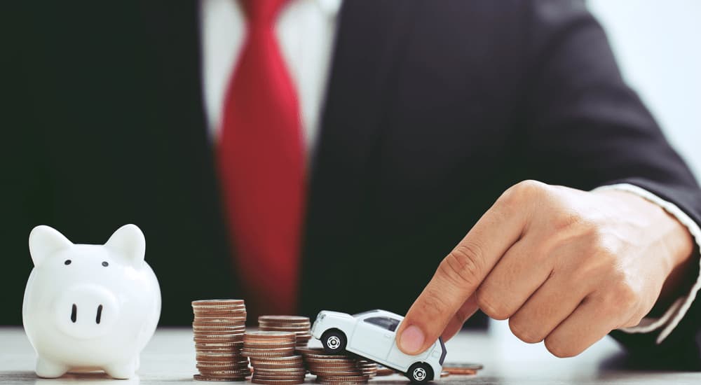 A car salesman is shown holding a toy car next to a stack of coins.