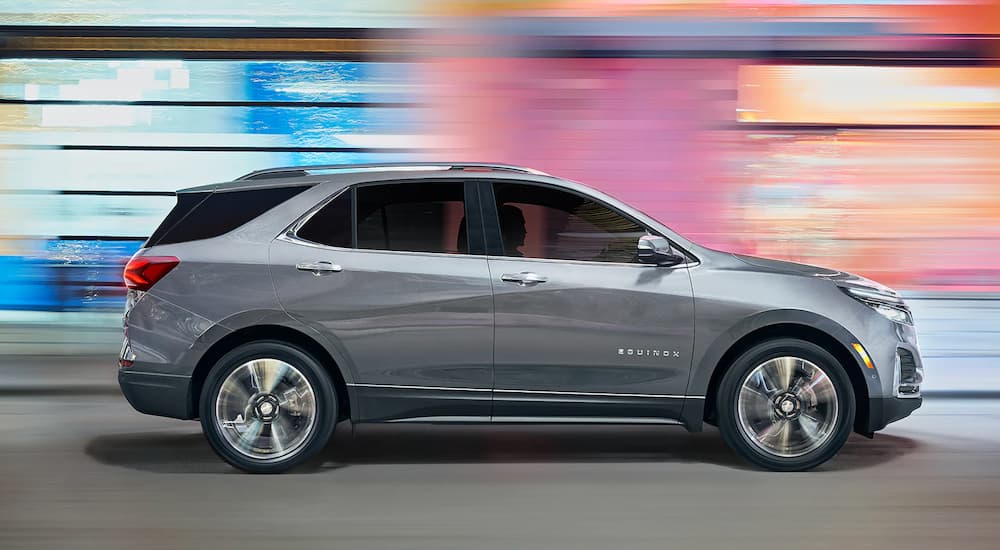 A silver 2023 Chevy Equinox is shown from the side driving on a brightly lit city street.
