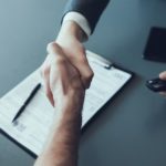 A salesman and a customer are shown shaking hands at a dealer that handles buy here pay here near me.