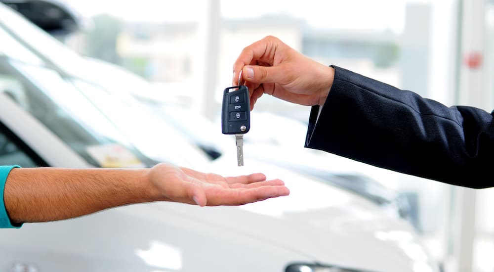 Keys are shown exchanging hands at a car dealership.