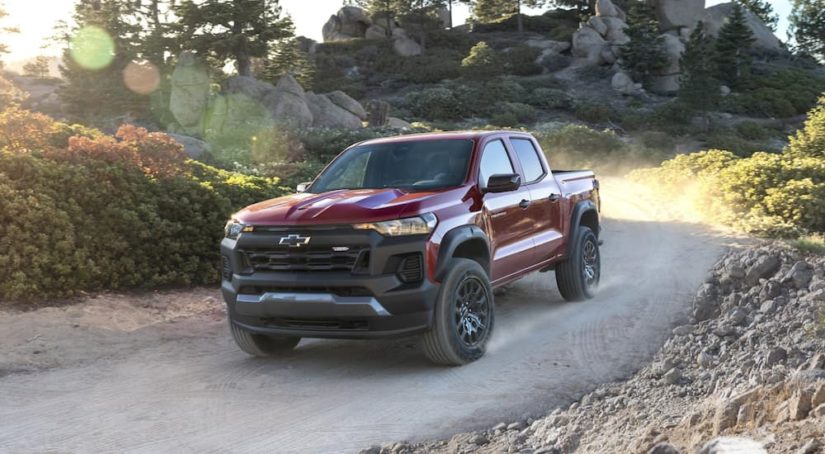 A maroon 2023 Chevy Colorado Trail Boss is shown driving on a dirt road.