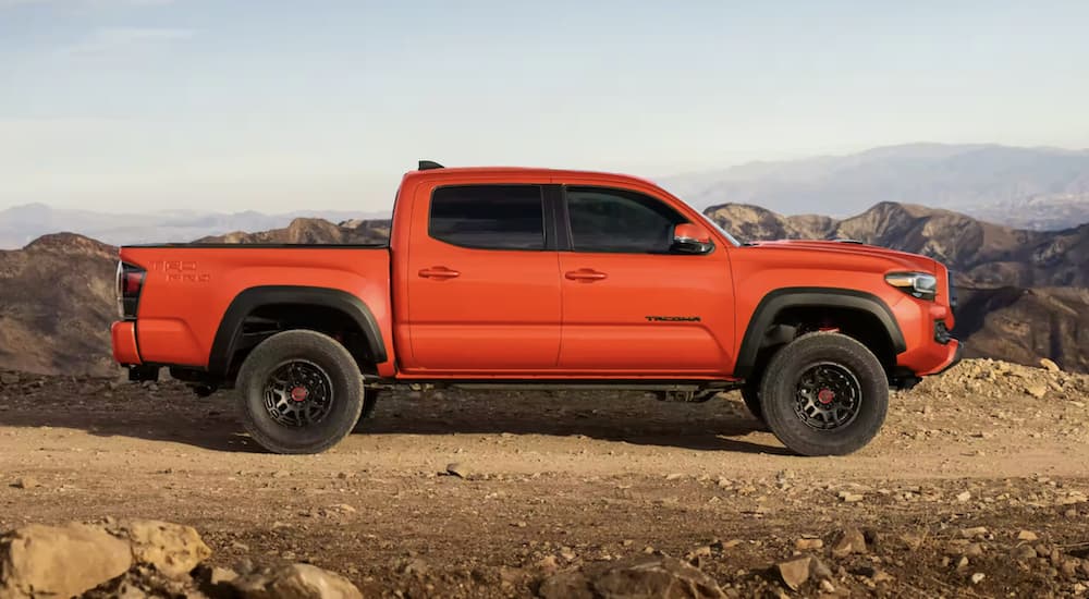 An orange 2023 Toyota Tacoma TRD is shown from the side parked on a dirt road.