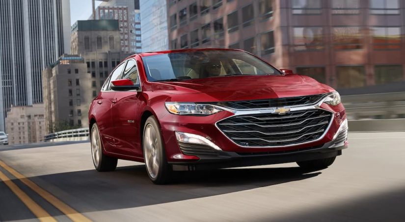 A red 2023 Chevy Malibu is shown driving on a city street.