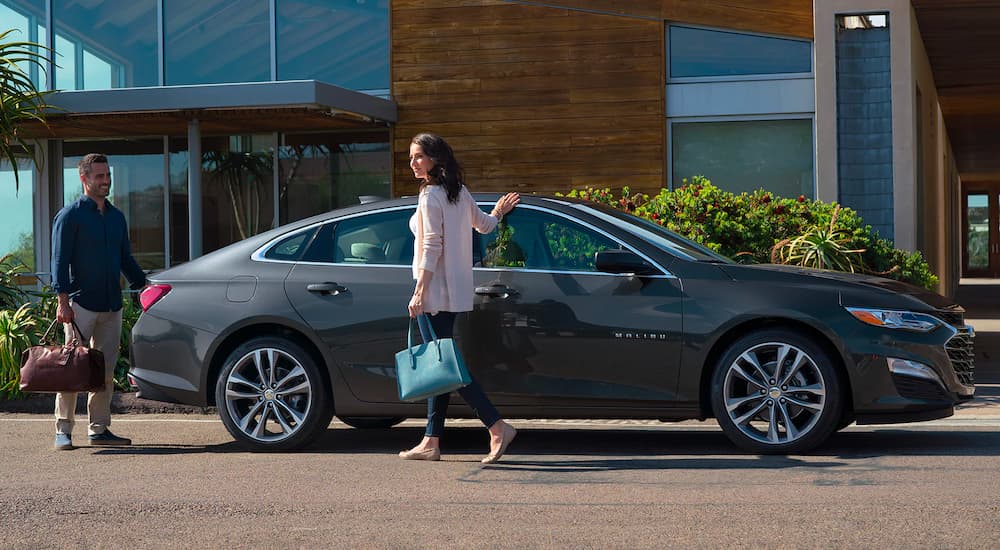 A couple is shown next to a grey 2023 Chevy Malibu.