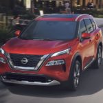 A red 2023 Nissan Rogue is shown from the front driving on an open road.