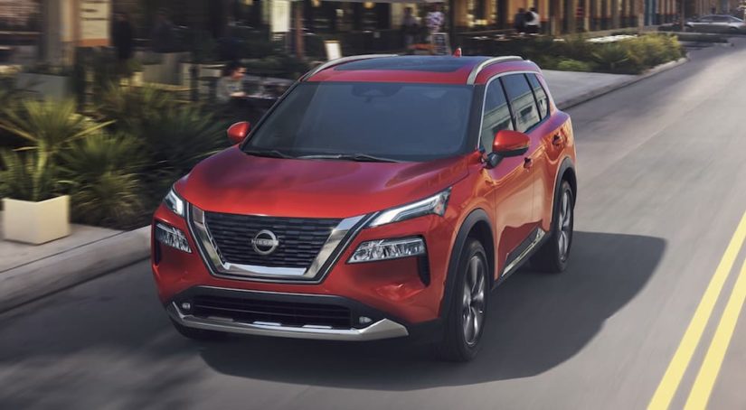 A red 2023 Nissan Rogue is shown from the front driving on an open road.