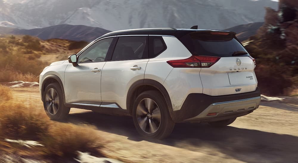 A white 2023 Nissan Rogue is shown from the rear driving on a dirt road.
