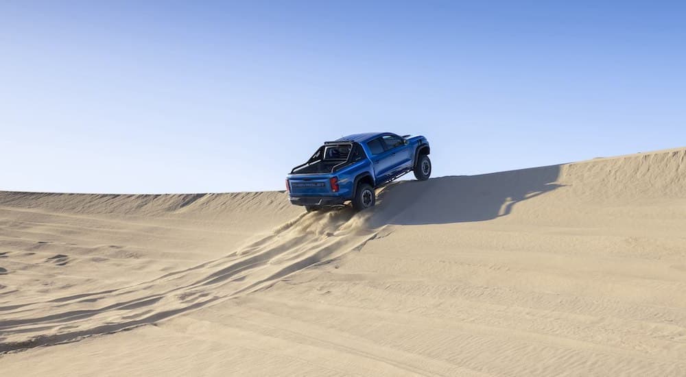 A blue 2023 Chevy Colorado ZR2 Desert Boss is shown from the rear while going over a sand dune.