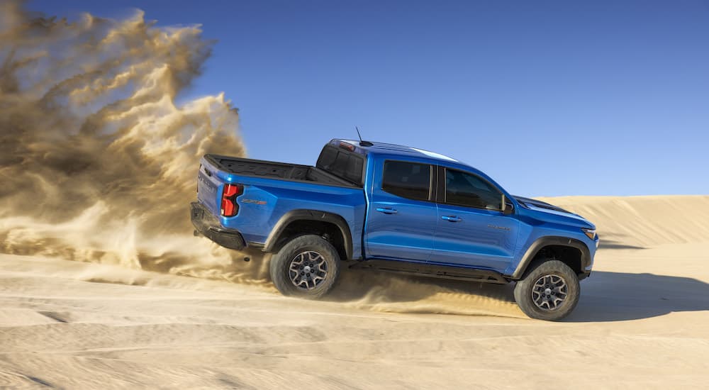 A blue 2023 Chevy Colorado ZR2 is shown from the side while driving on a sand dune.