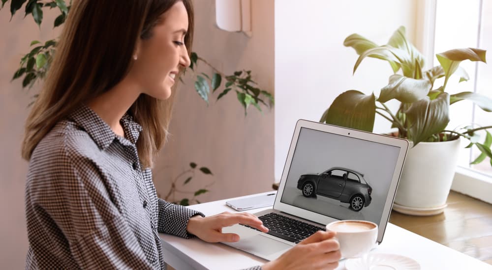 A woman is shown looking at different vehicle's on a laptop.