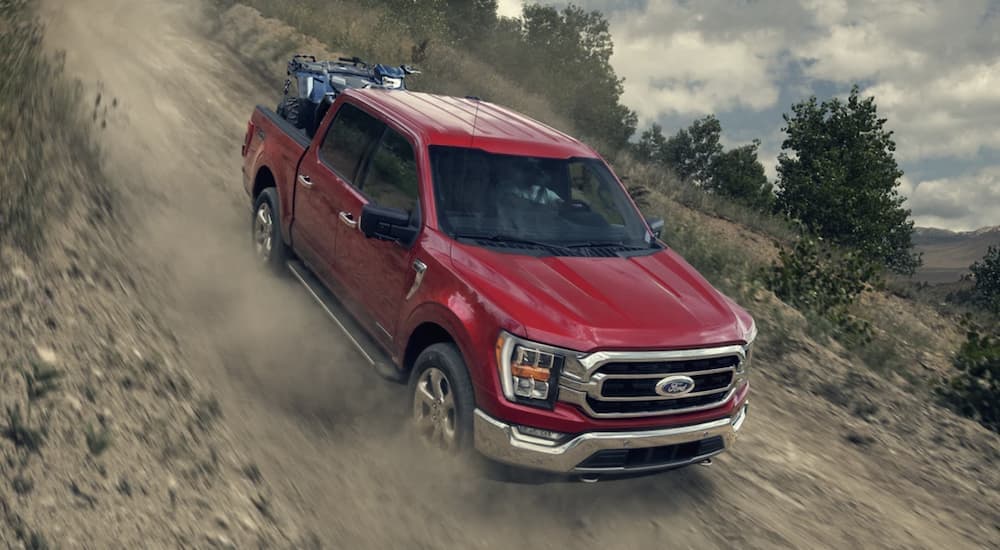 A red 2023 Ford F-150 is shown driving down a steep dirt road.
