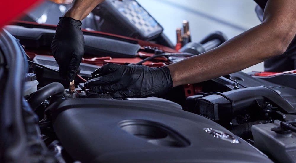 A close up shows a mechanic working on a Mazda engine.