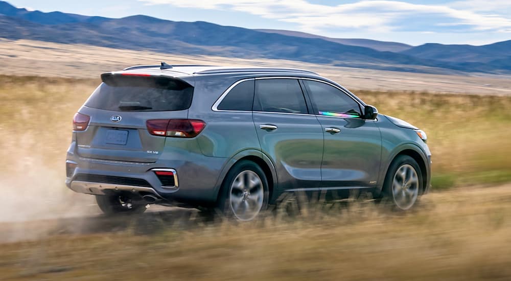 A grey 2020 Kia Sorento is shown from a rear angle driving through a grassy field.