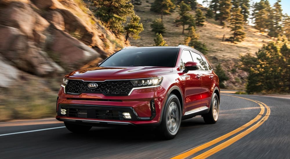 A red 2021 Kia Sorento is shown driving on a winding road by a rocky mountain.