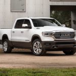 One of many cars for sale in Oklahoma City, a white 2020 Ram 1500, is shown from the front parked in front of a warehouse.