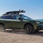 A green 2021 Subaru Outback is shown from the side while driving down the beach.