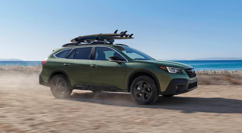 A green 2021 Subaru Outback is shown from the side while driving down the beach.