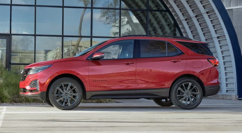 A red 2023 Chevy Equinox RS is shown from the side parked in front of a modern building.