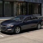A grey 2023 Chevy Malibu is shown parked on the side on a city street.