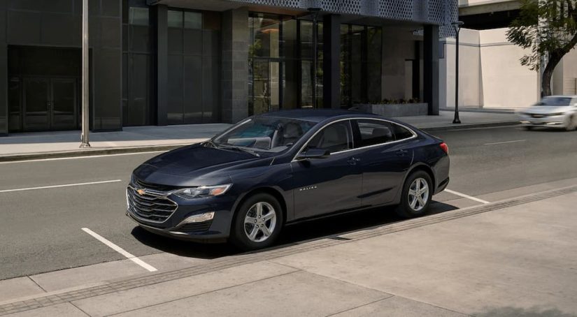 A grey 2023 Chevy Malibu is shown parked on the side on a city street.