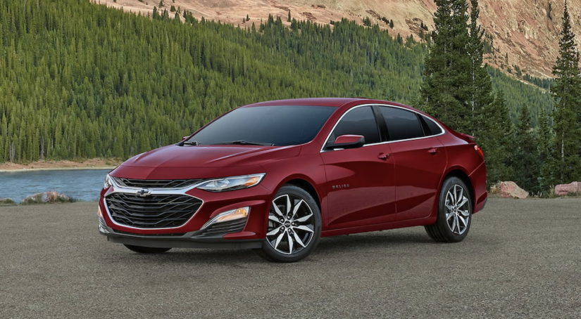 A red 2023 Chevy Malibu is shown from the side parked in front of a forest.
