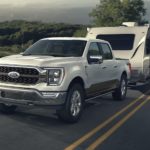 A white 2023 Ford F-150 is shown towing a trailer on an open road.
