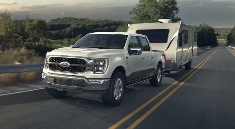 A white 2023 Ford F-150 is shown towing a trailer on an open road.