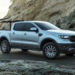 A person is shown loading a surfboard on a silver 2023 Ford Ranger Sport.
