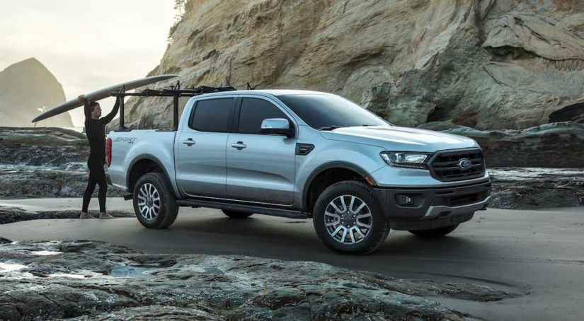 A person is shown loading a surfboard on a silver 2023 Ford Ranger Sport.