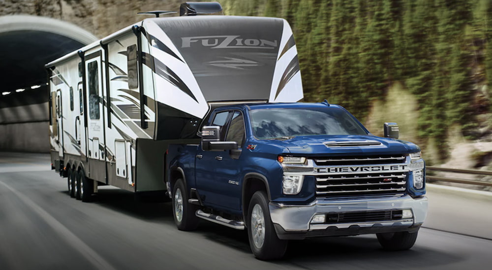 A blue 2023 Chevrolet Silverado 2500 HD is shown towing a trailer on an open road.