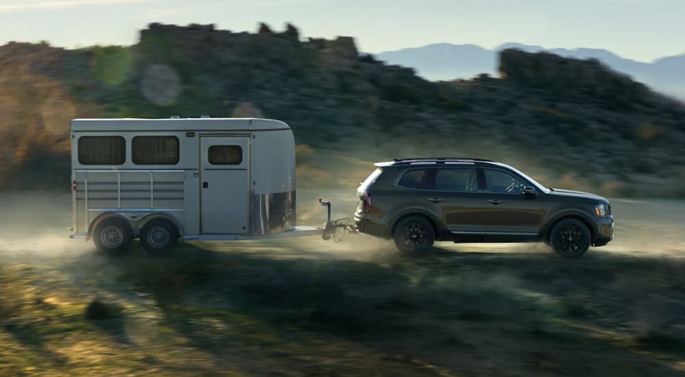 A grey 2023 Kia Telluride X-Pro is shown towing a trailer on an open road.