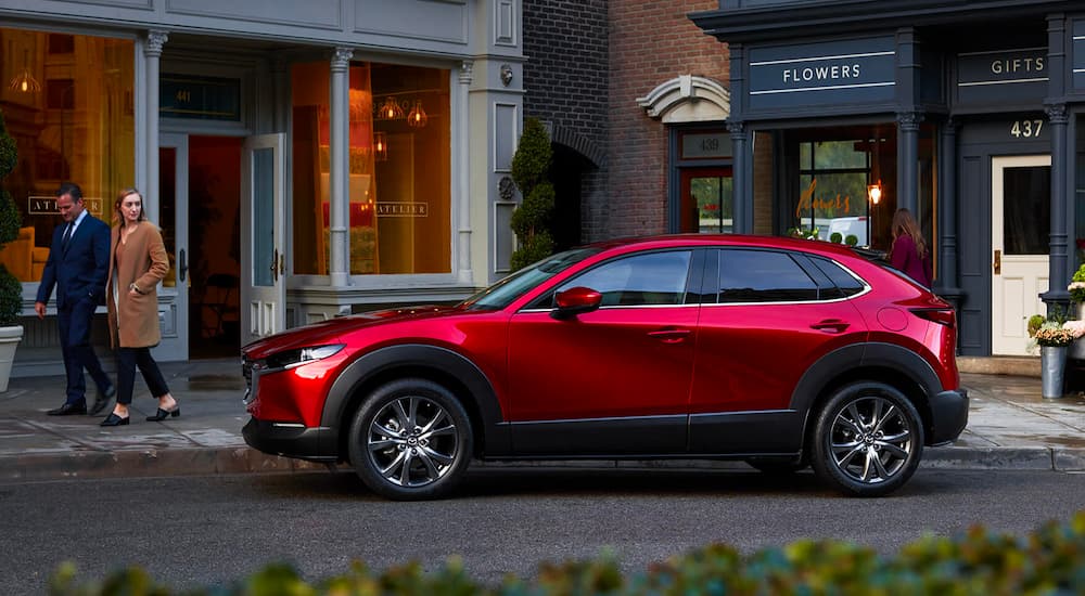 A red 2023 Mazda CX-30 is shown parked on a city street in front of shops.