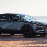 A grey 2023 Mazda CX-30 is shown driving on a path overlooking the ocean.