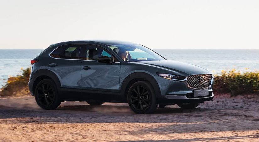 A grey 2023 Mazda CX-30 is shown driving on a path overlooking the ocean.