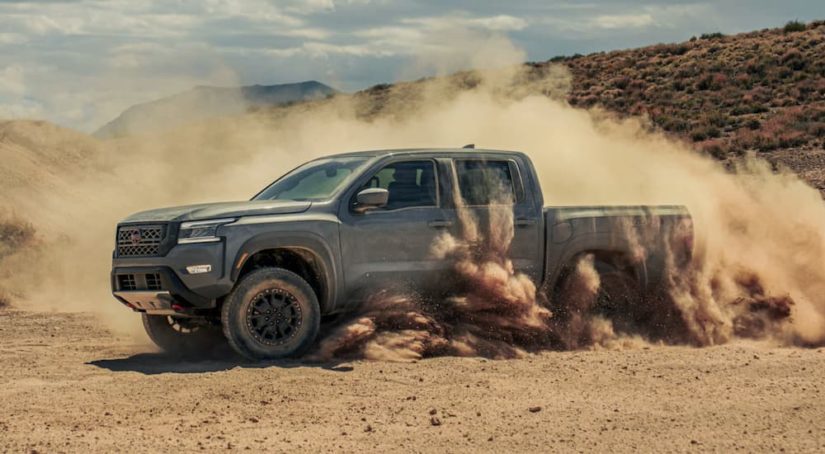 A grey 2023 Nissan Frontier Pro4x is shown off-roading and kicking up dirt.
